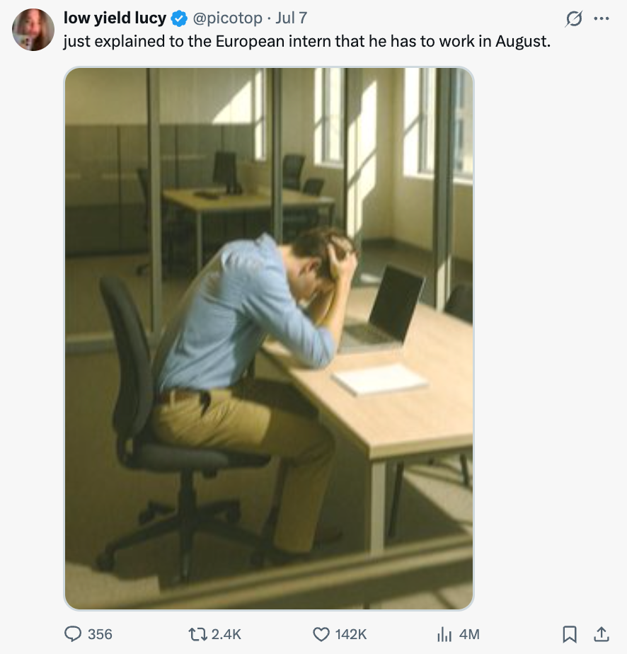 Person in an office sits at a desk with head in hands next to a laptop, appearing stressed