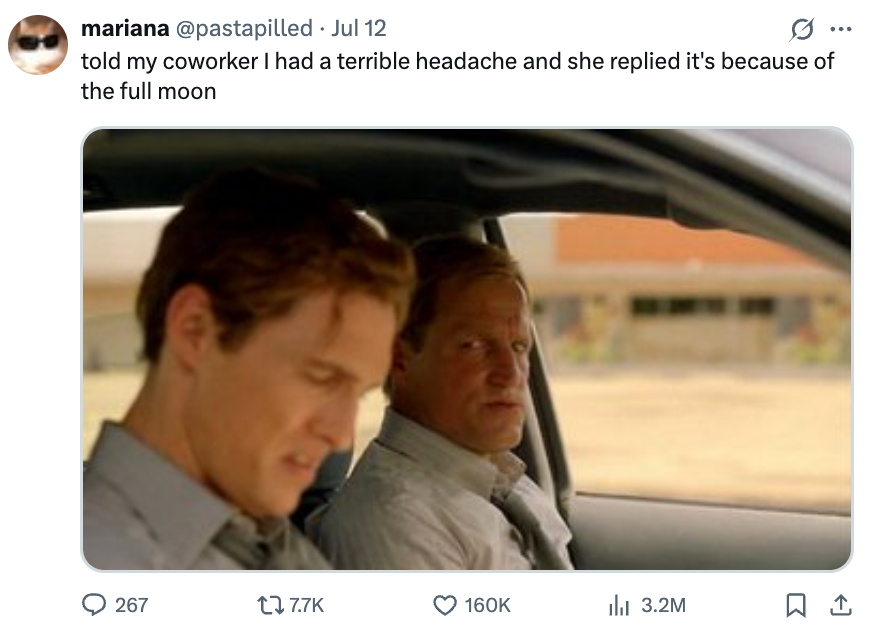 Two men sit in a car, one looking forward with a serious expression