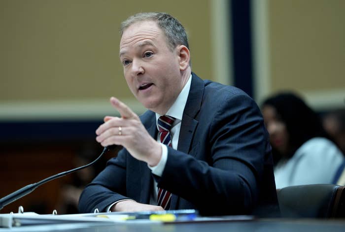 Person in a suit and tie speaks while gesturing at a public hearing or formal event