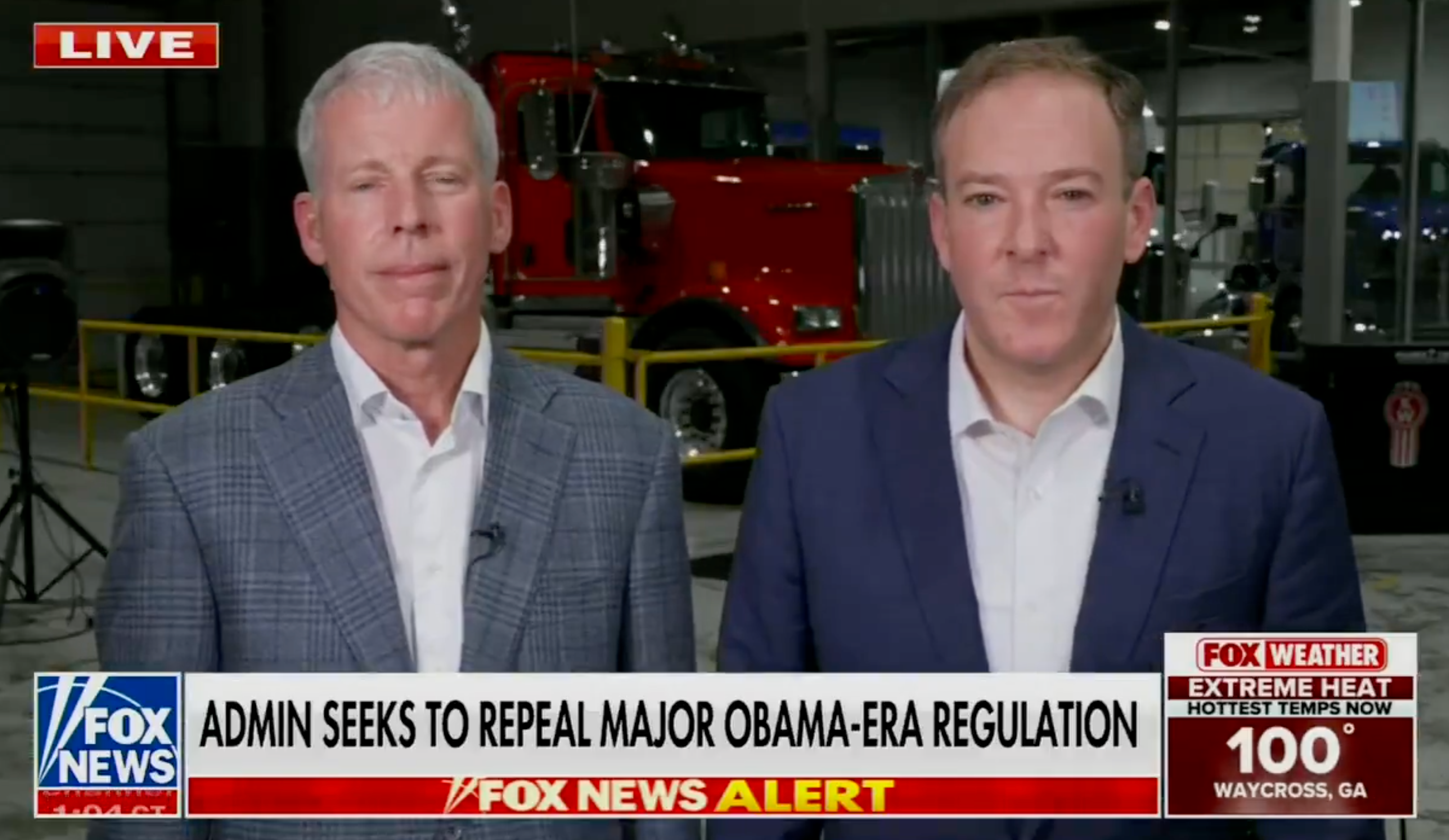 Two men in suits stand inside a studio with a large red truck in the background, during a live Fox News broadcast about Obama-era regulation changes