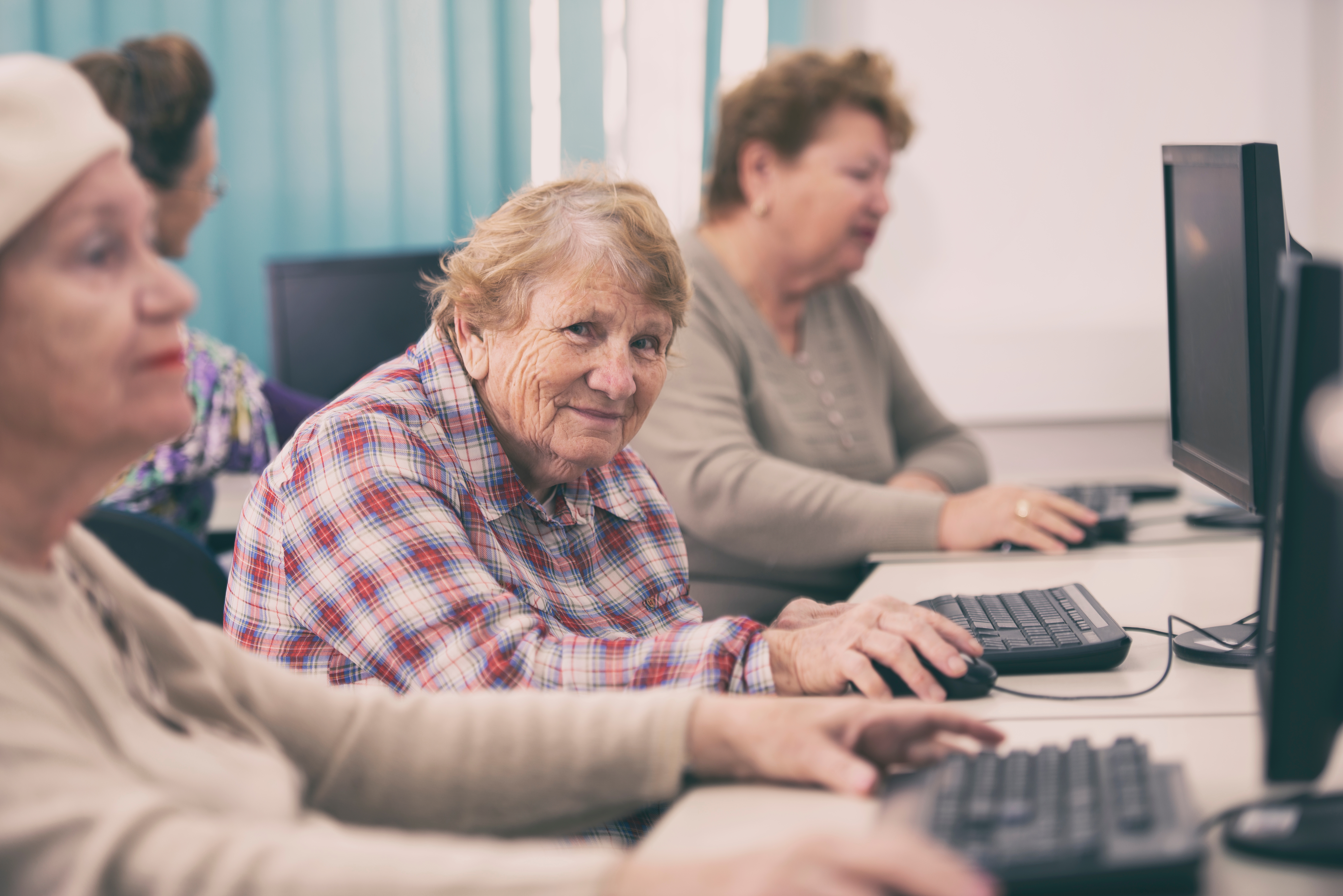 Elderly women seated at computers in a learning environment, focused on screens and keyboards