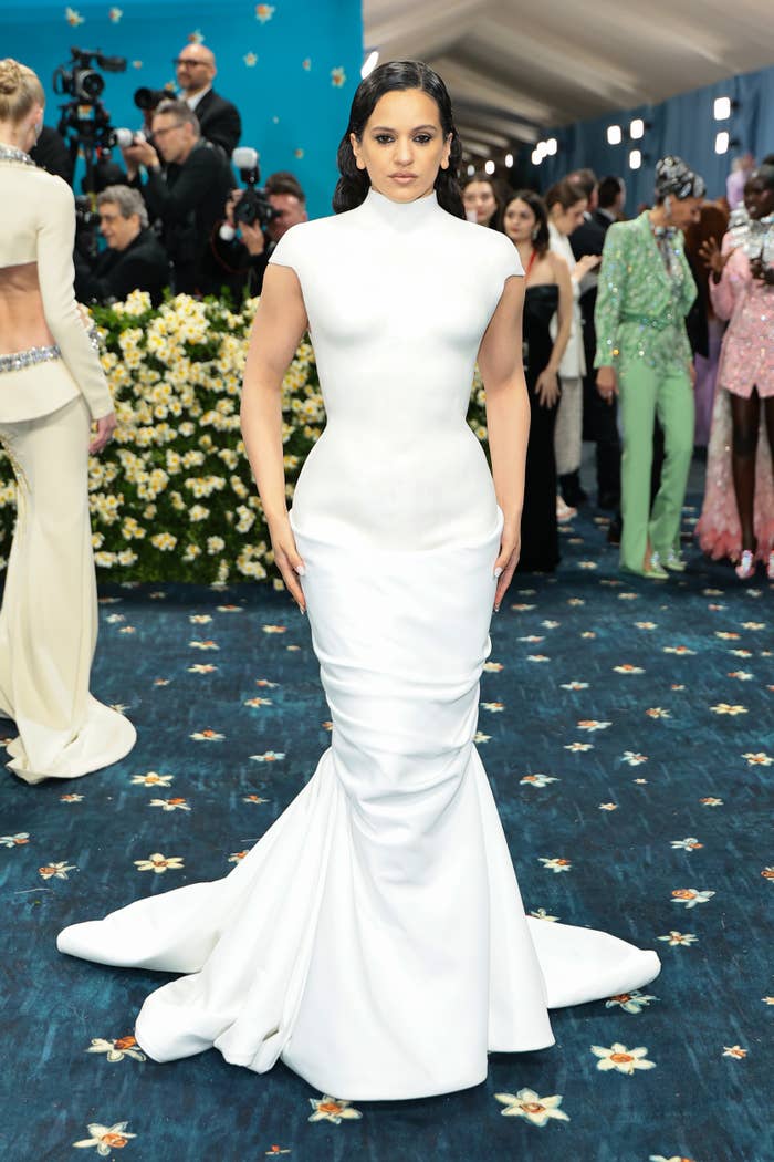 Person in sleek, form-fitting white gown at a formal event, surrounded by photographers and onlookers