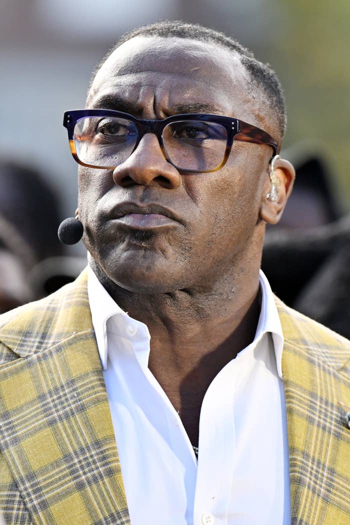 Person wearing glasses and a plaid jacket with a white shirt, speaking with a headset microphone