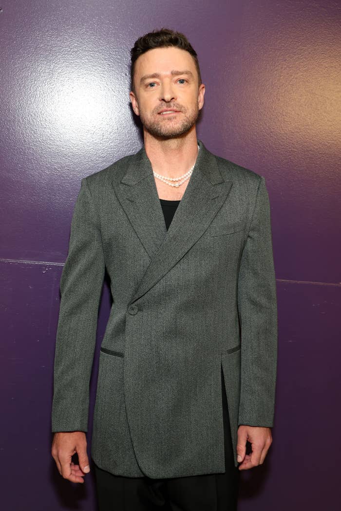 Justin Timberlake in a stylish double-breasted blazer with a pearl necklace, posing against a plain backdrop