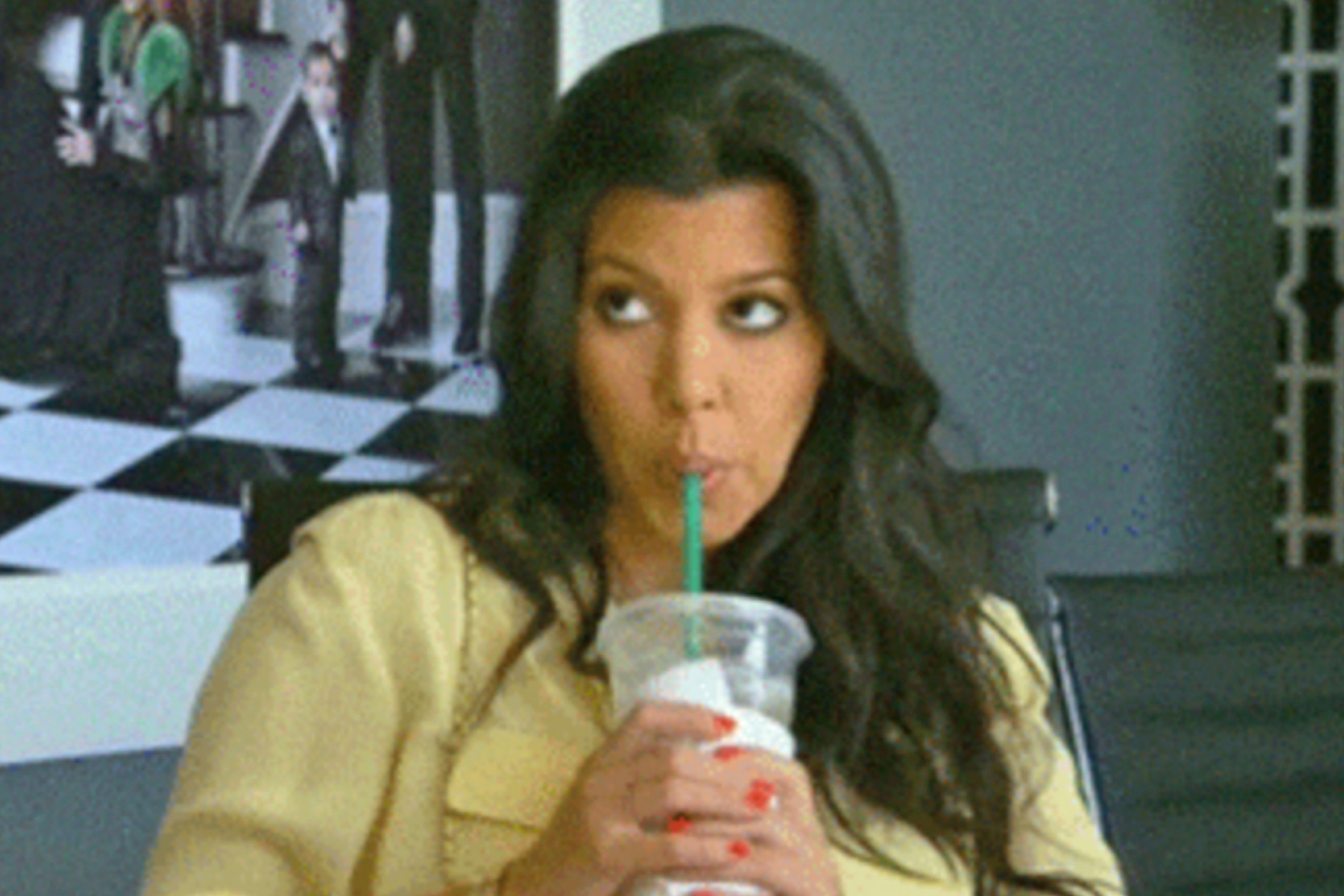 Kourtney Kardashian sipping from a straw, looking to the side, with long hair and wearing a casual outfit