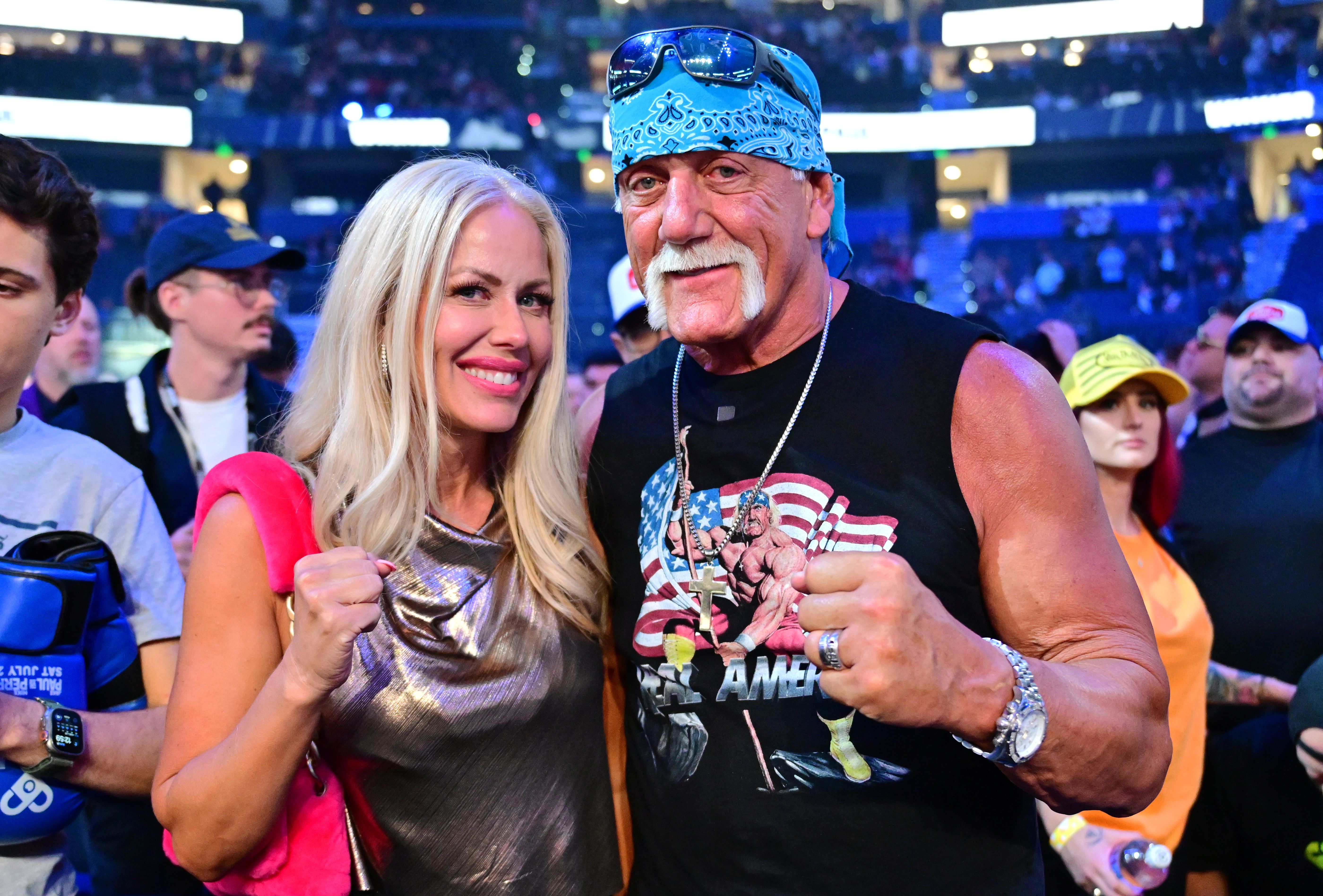 A man and woman in casual outfits pose with their fists raised at an indoor event, surrounded by a crowd