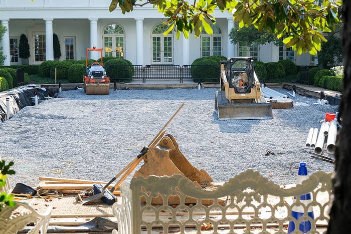 A construction site with heavy machinery preparing the ground in a garden setting outside a large white building