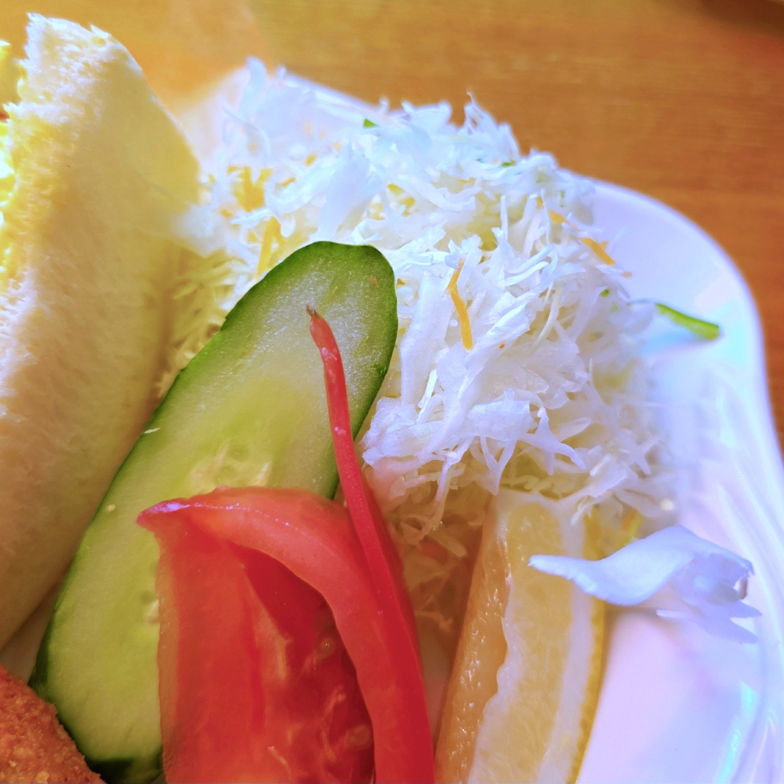 野菜サラダが盛り付けられた白い皿。キャベツ、キュウリ、トマトのスライスが見えます。