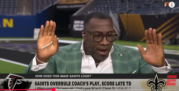 A person in a checkered suit is talking animatedly on a sports show set. There&#x27;s text about a controversial Saints versus Falcons game play