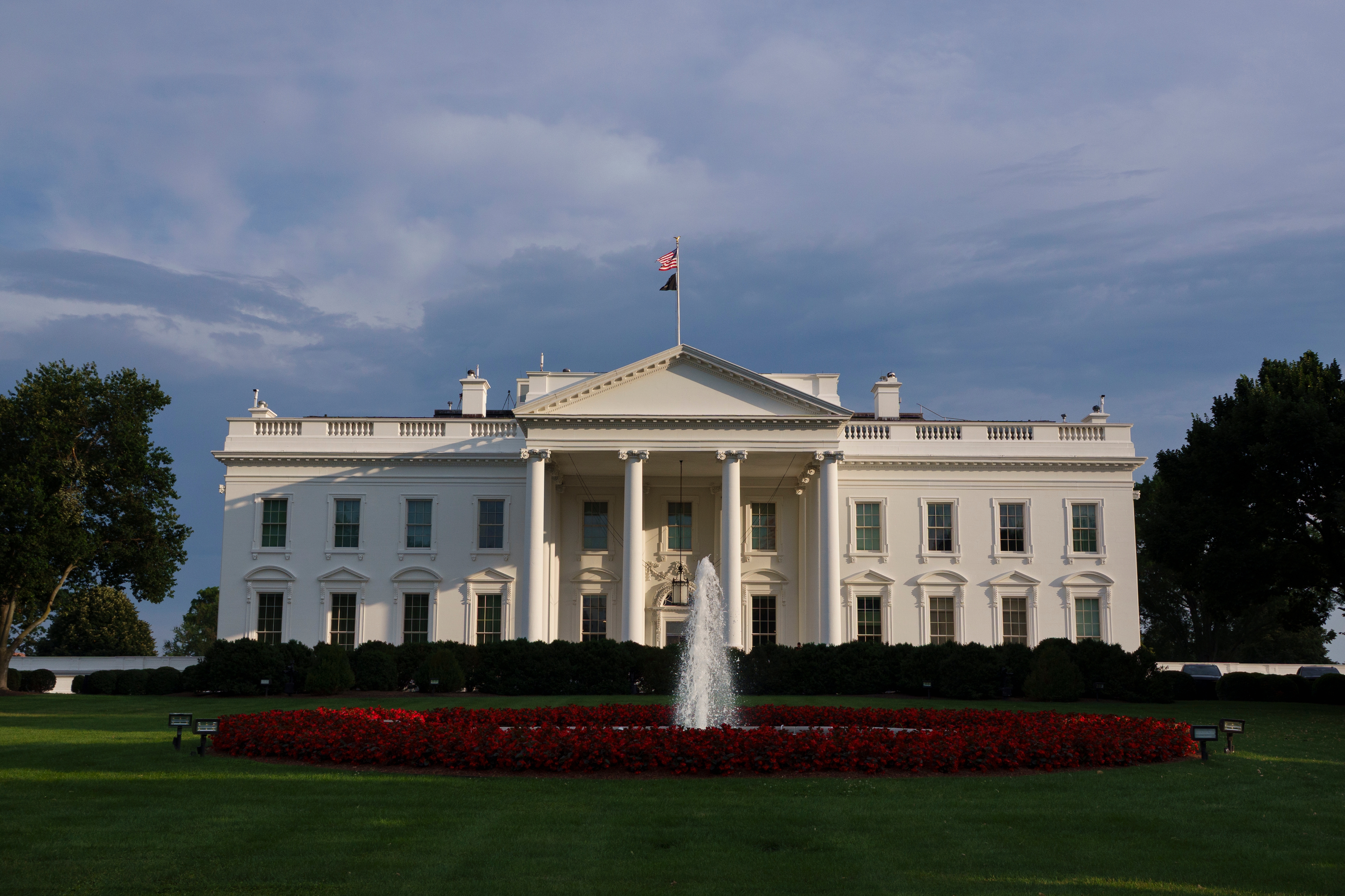 The White House with a fountain in front and a well-maintained lawn, under a cloudy sky