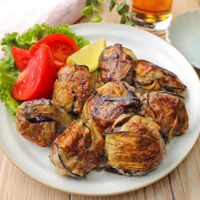 ナスとひき肉を巻いた焼き料理が皿に盛られ、トマトとレタス、レモンが添えられています。