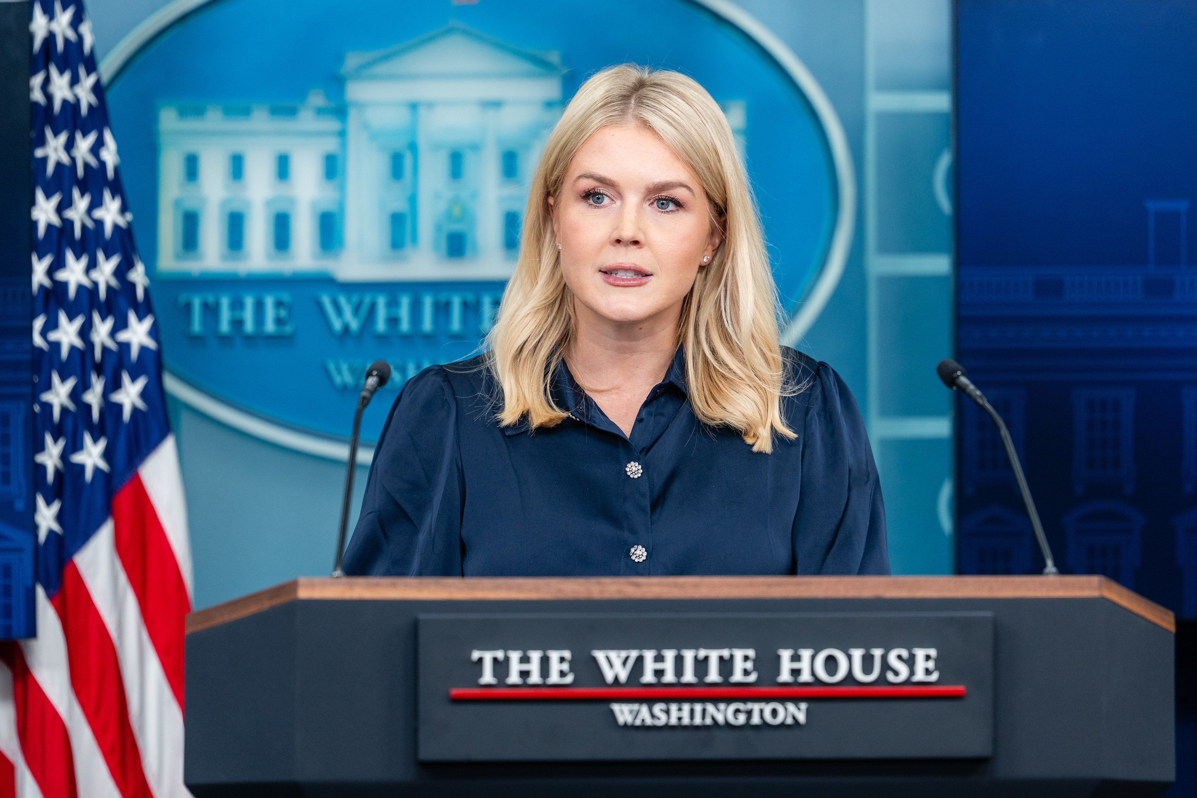 A person speaks at a podium with &quot;The White House&quot; sign and emblem in the background