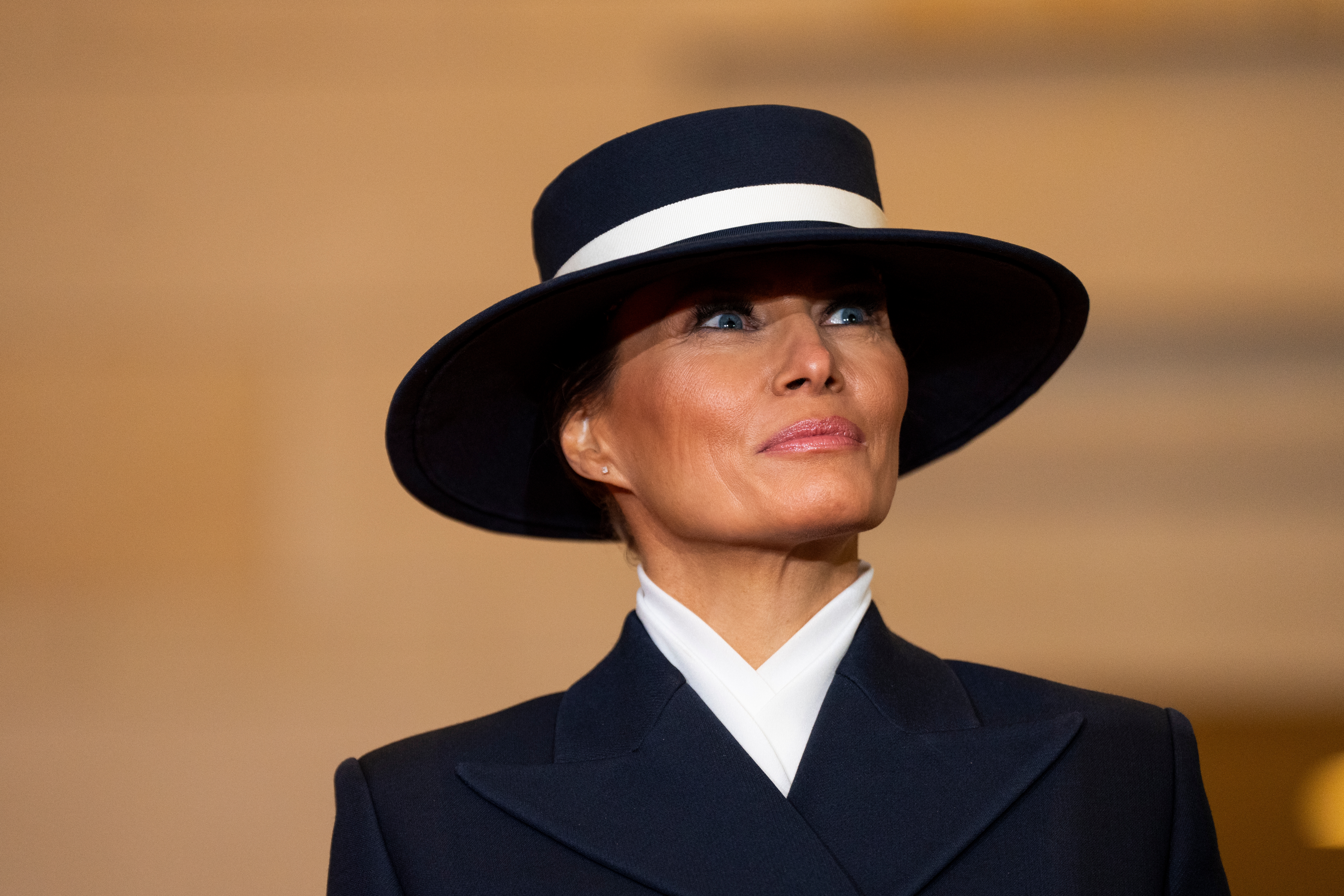 Person in a wide-brimmed hat and tailored suit, looking upwards with a neutral expression