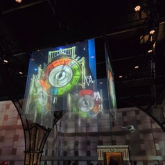 Exhibición interactiva con proyecciones de relojes gigantes, luces y estructuras arquitectónicas bajo un techo oscuro