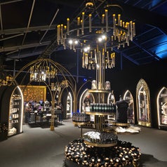 Exhibición temática con decoración gótica, luces colgantes, arcos y estantes con productos expuestos; ambiente elegante y sofisticado