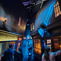 Personas recorren un callejón temático oscuro con tiendas iluminadas, evocando un ambiente mágico y misterioso