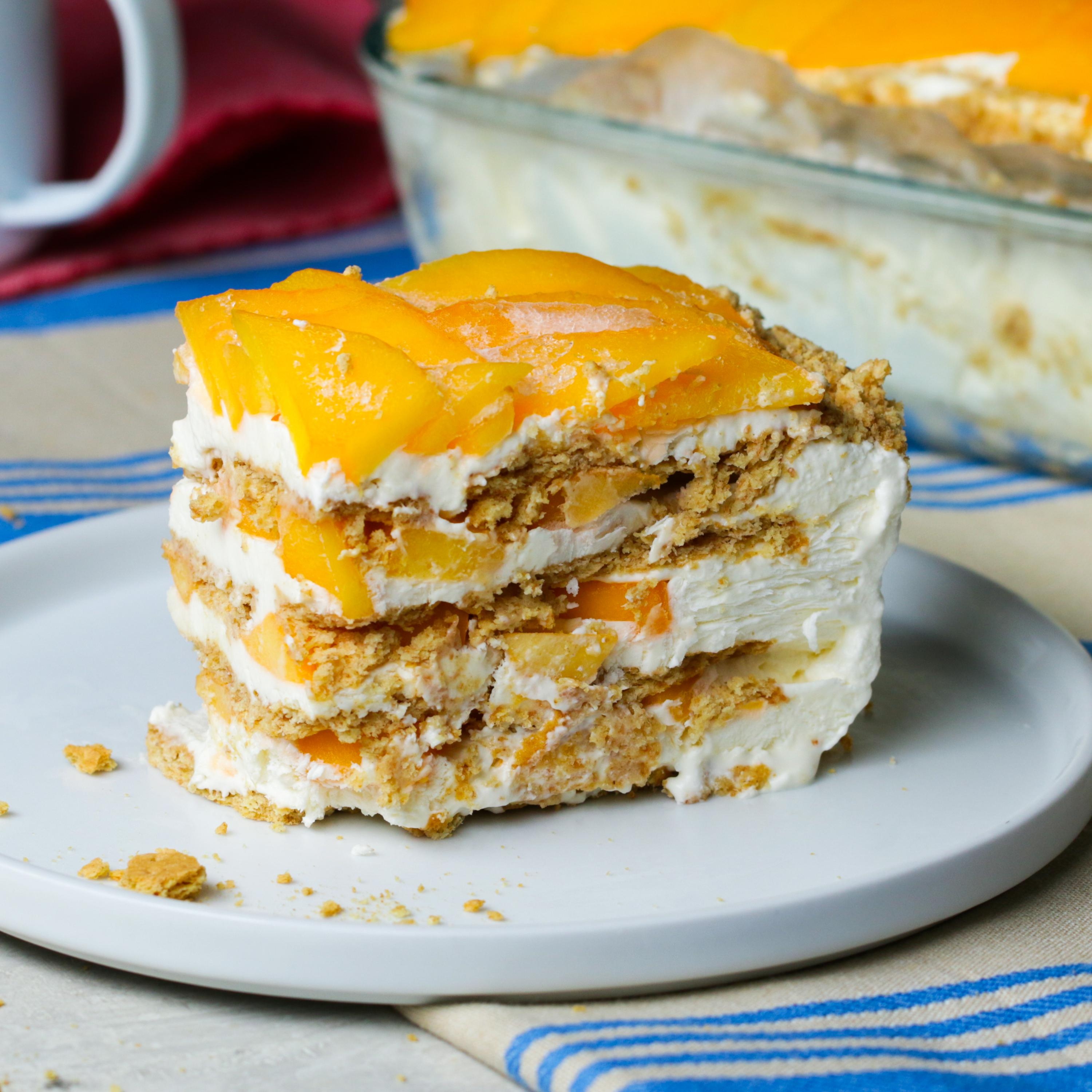 Slice of mango icebox cake with layers of cream and graham crackers on a white plate, set on a striped cloth