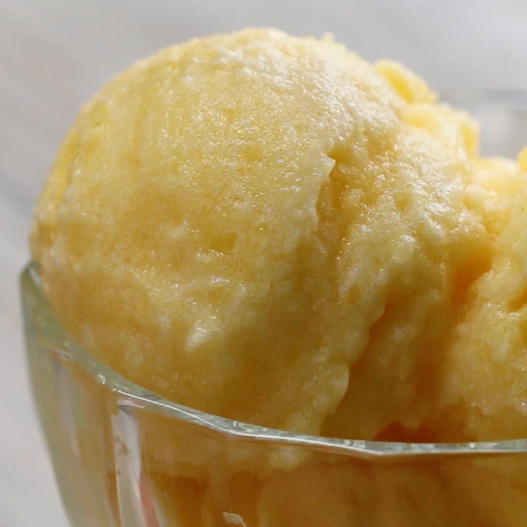 A scoop of creamy, smooth yellow-colored sorbet served in a glass dish, suggesting a refreshing dessert