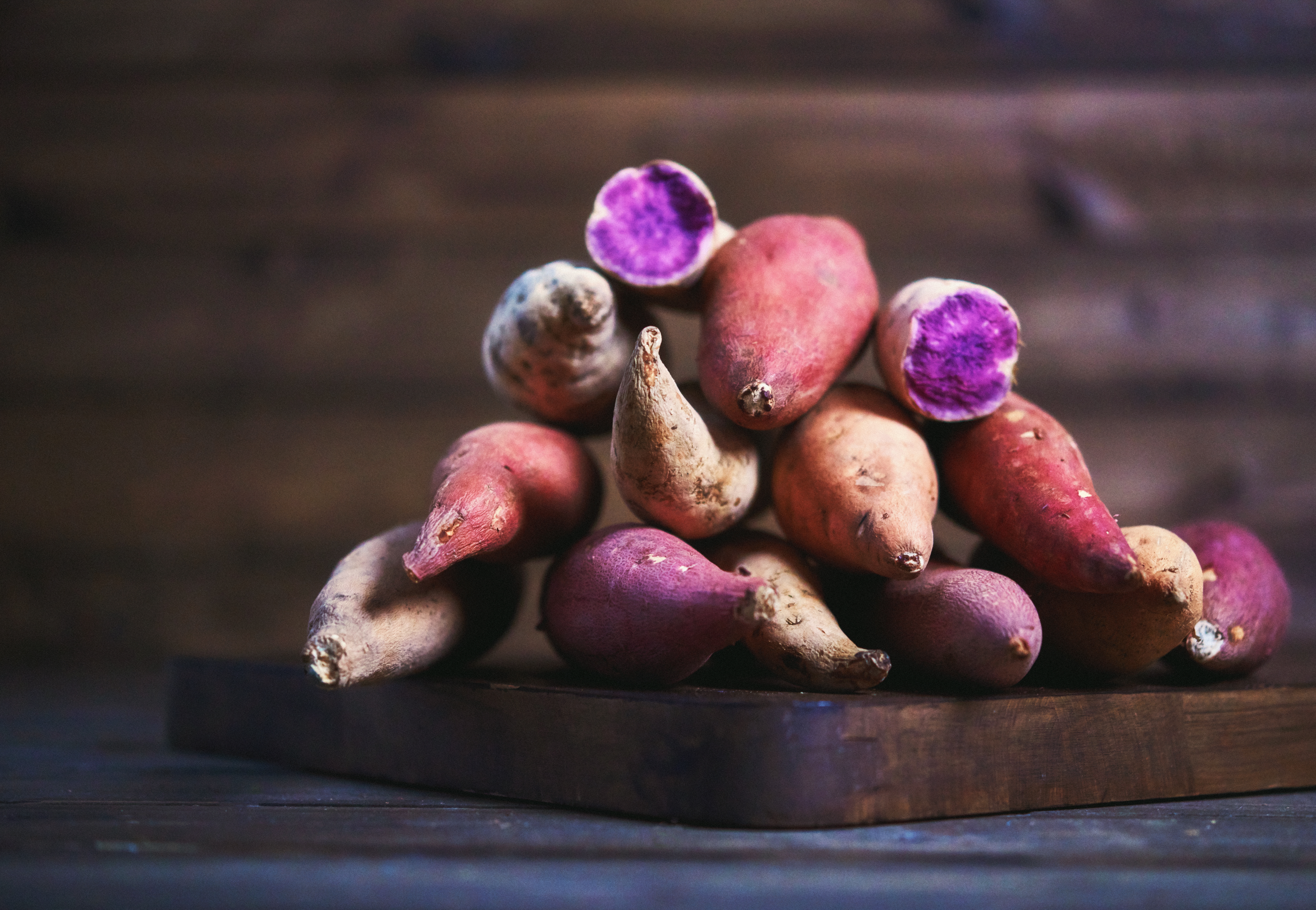 Assorted sweet potatoes, including purple-fleshed ones, piled on a wooden board
