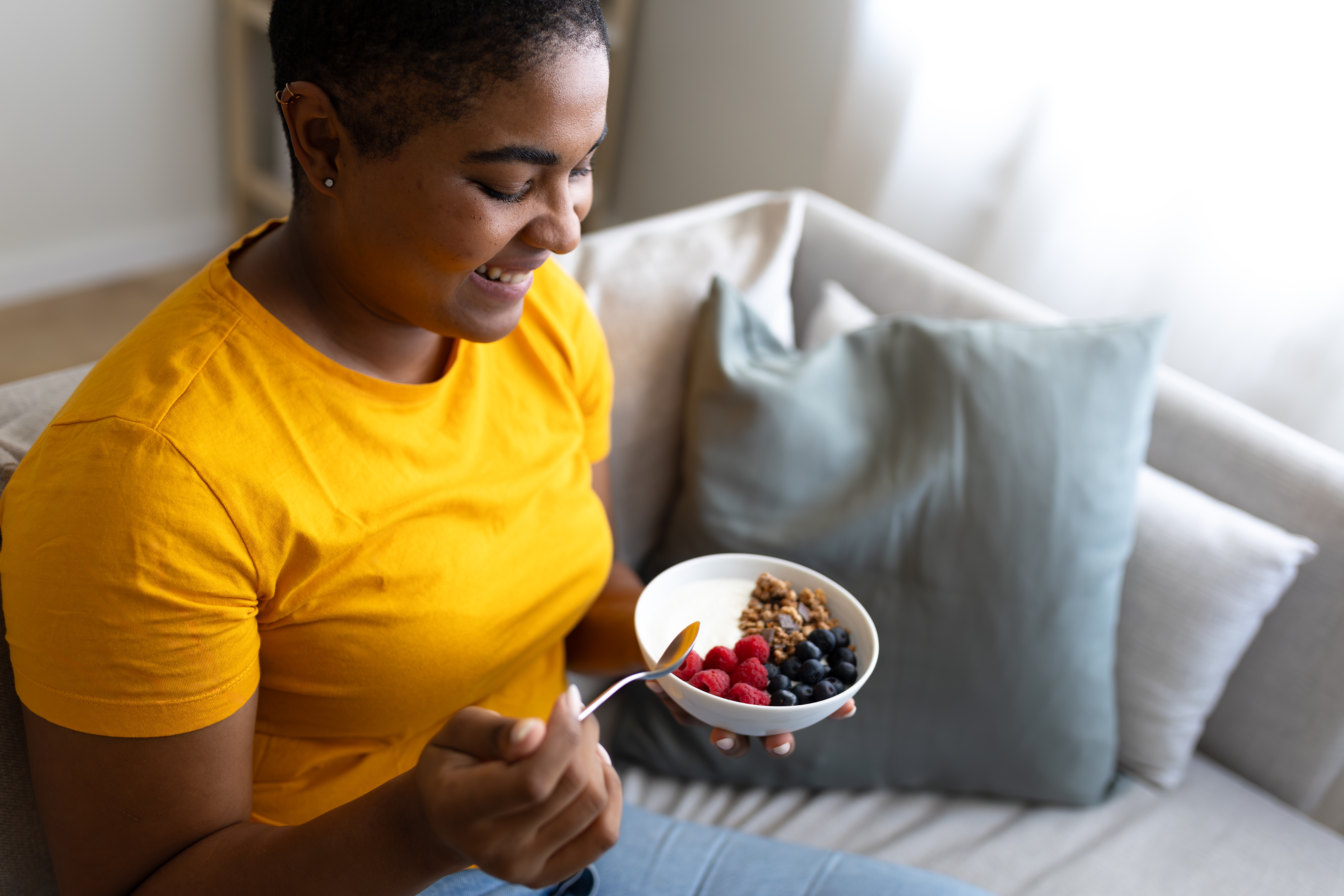 Person smiling while holding a bowl of assorted berries and nuts on a couch