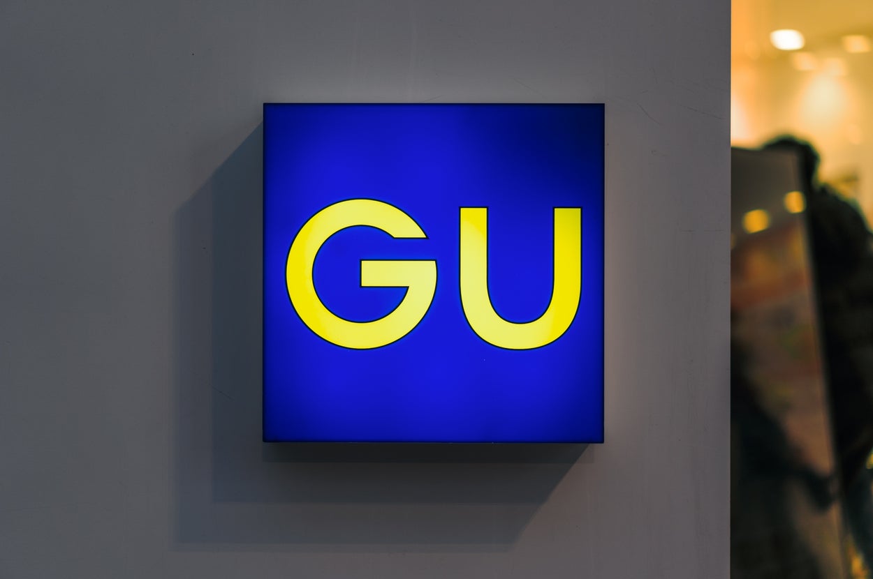 Illuminated sign with the letters "GU" in yellow on a blue background, mounted on a wall