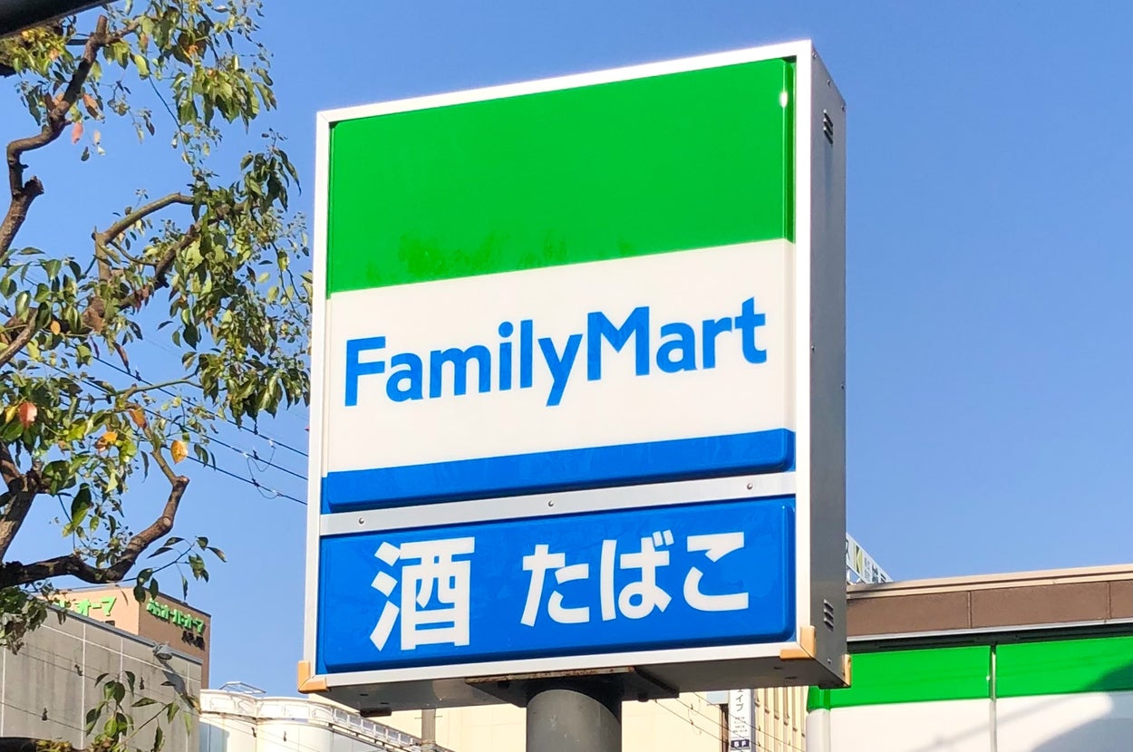 ファミリーマートの看板。「酒」「たばこ」と書かれた文字が見える。背景には木と建物がある。