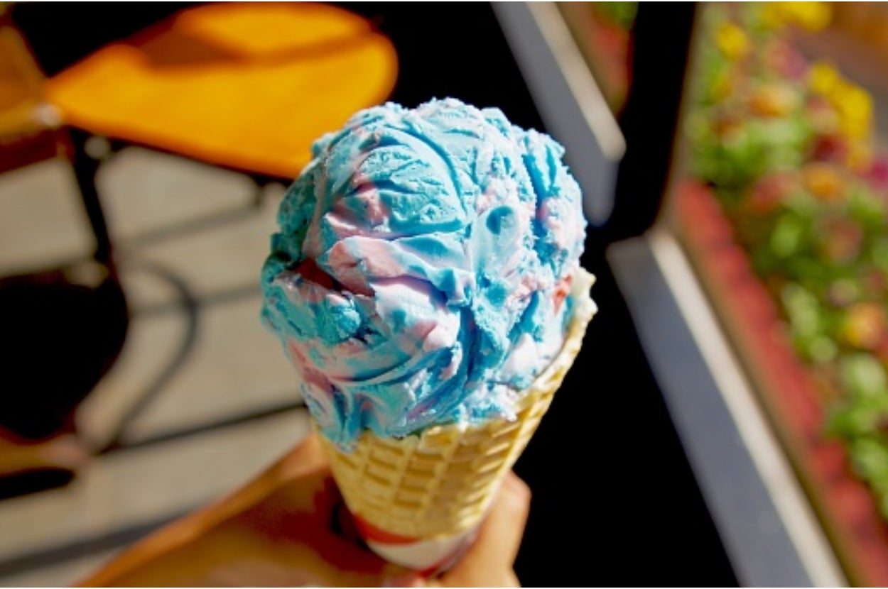 Person holding a waffle cone with blue and pink swirled ice cream, outdoors