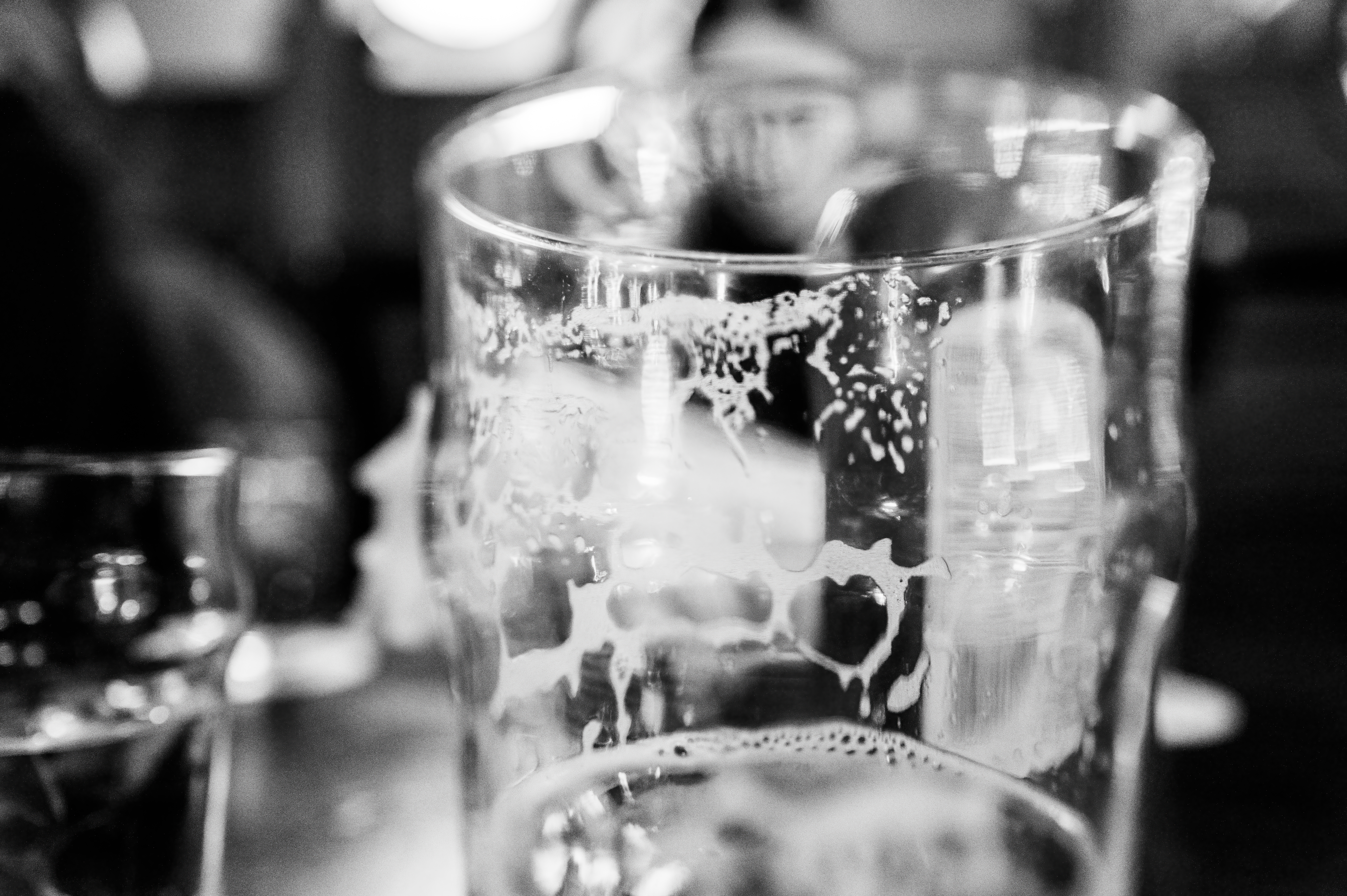 Close-up of an empty, frosty pint glass with beer foam remnants at a lively pub setting. Blurred background shows a cozy, bustling atmosphere
