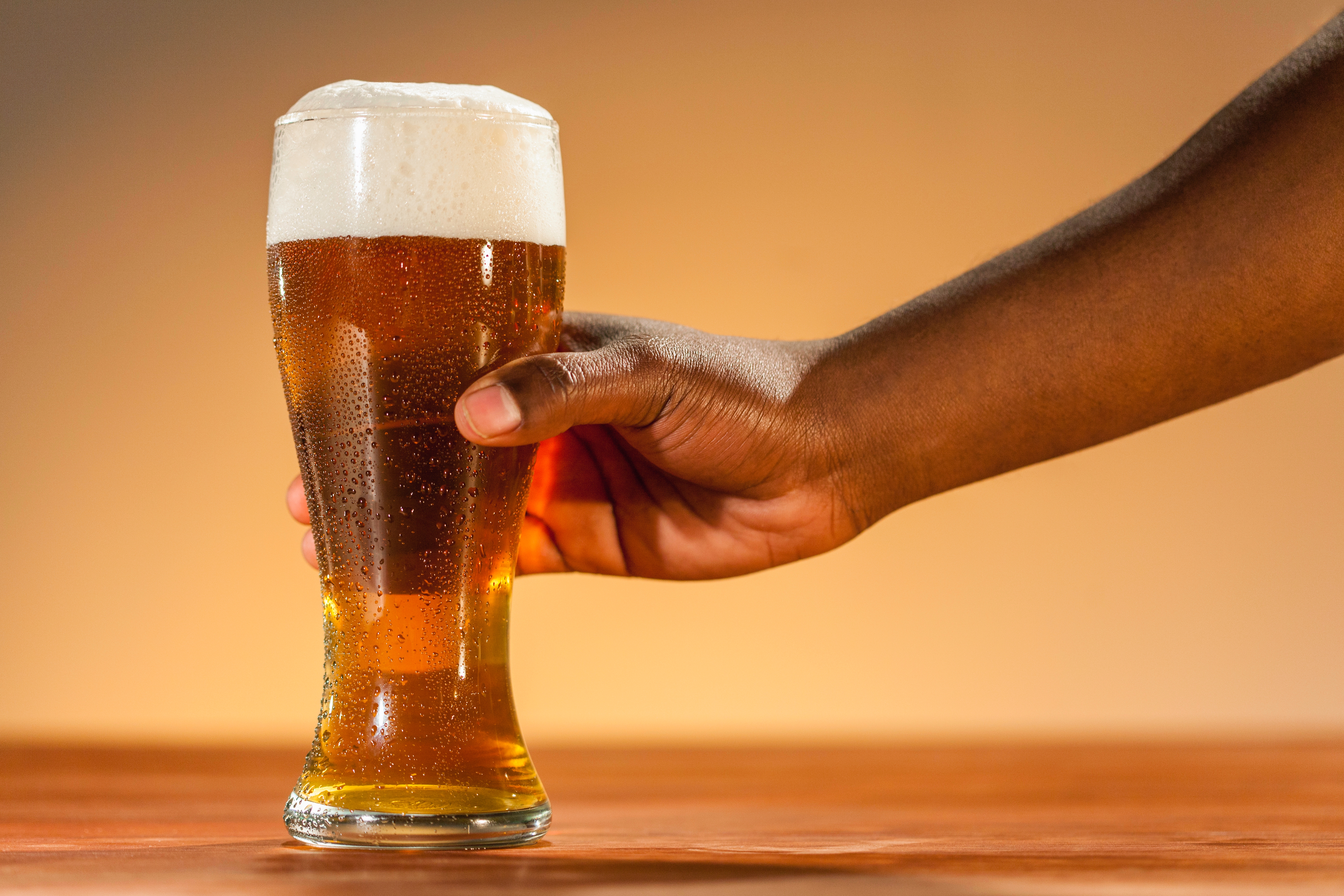 A hand holding a frothy glass of beer on a wooden surface