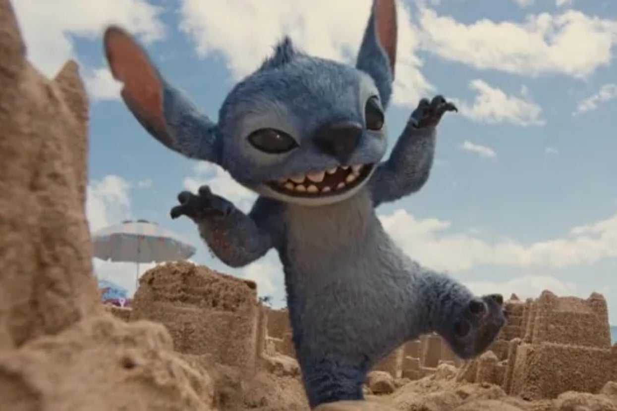 Stitch, a blue alien character, joyfully plays among sandcastles on a sunny beach