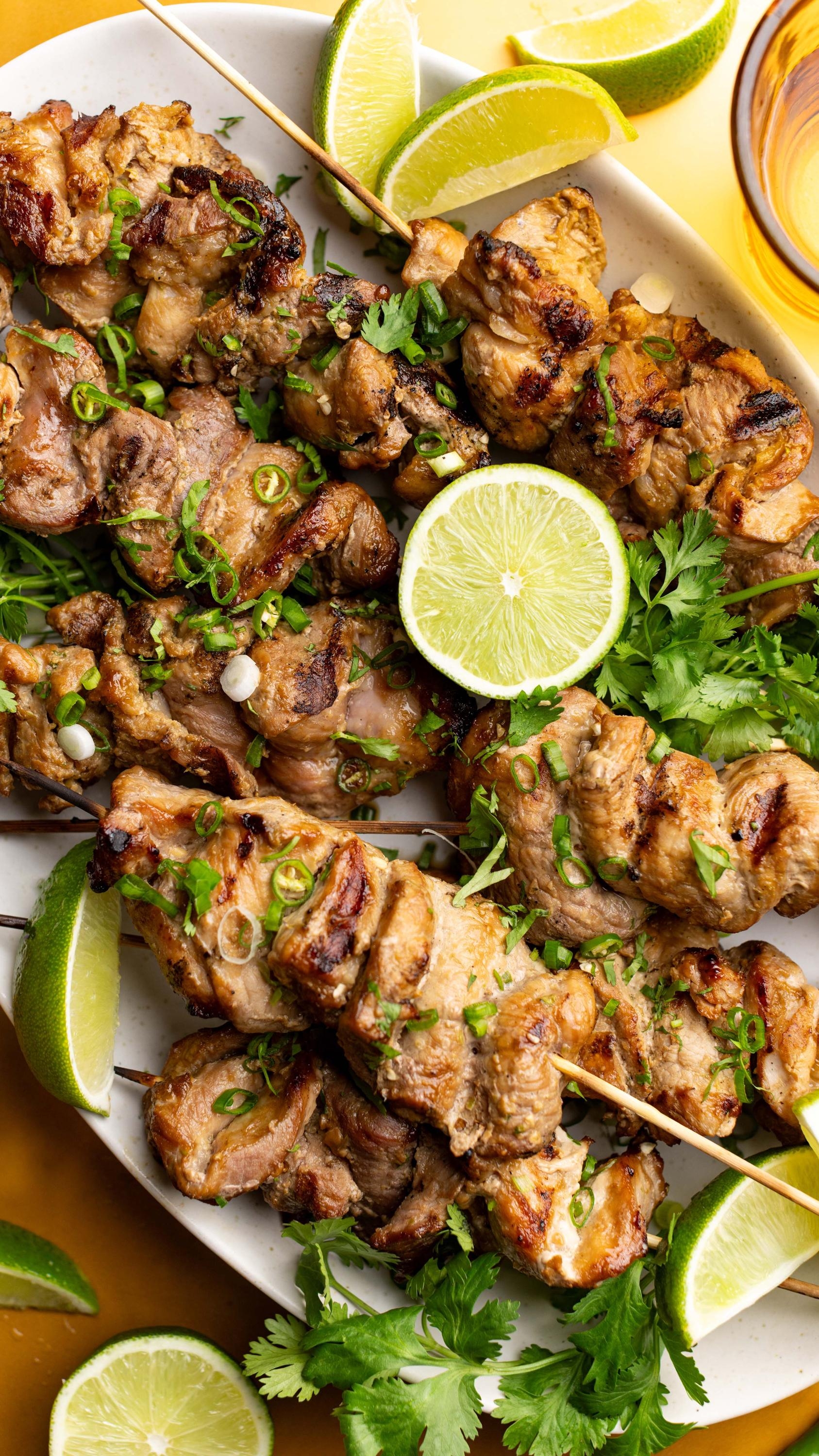 Grilled meat skewers garnished with lime slices and fresh herbs on a platter