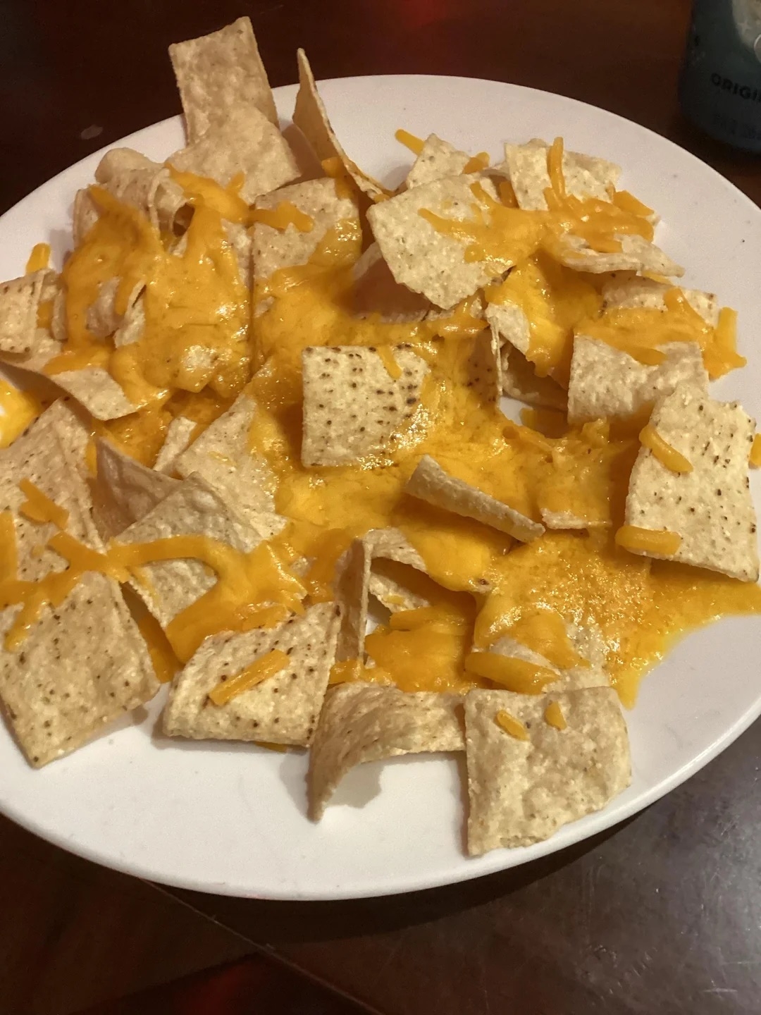 A plate of tortilla chips covered with melted cheese, resembling nachos, served on a white dish