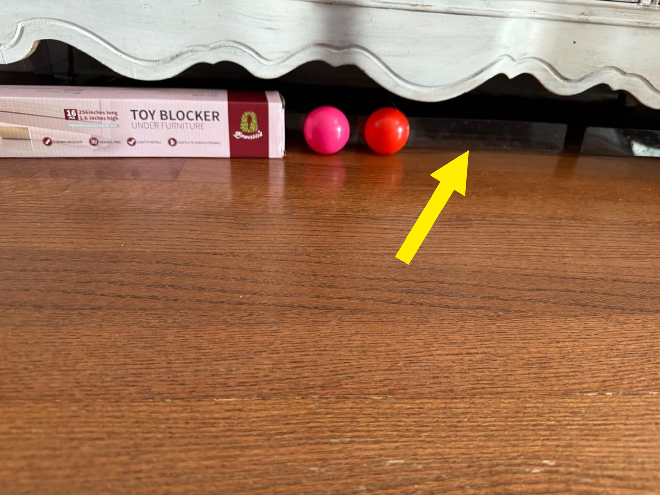 Toy blocker is wedged nether  furnishings  alongside 2  tiny  balls connected  a woody  floor, preventing toys from rolling underneath