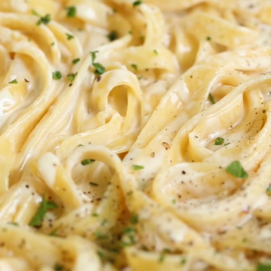 Close-up of creamy fettuccine alfredo pasta garnished with herbs and black pepper