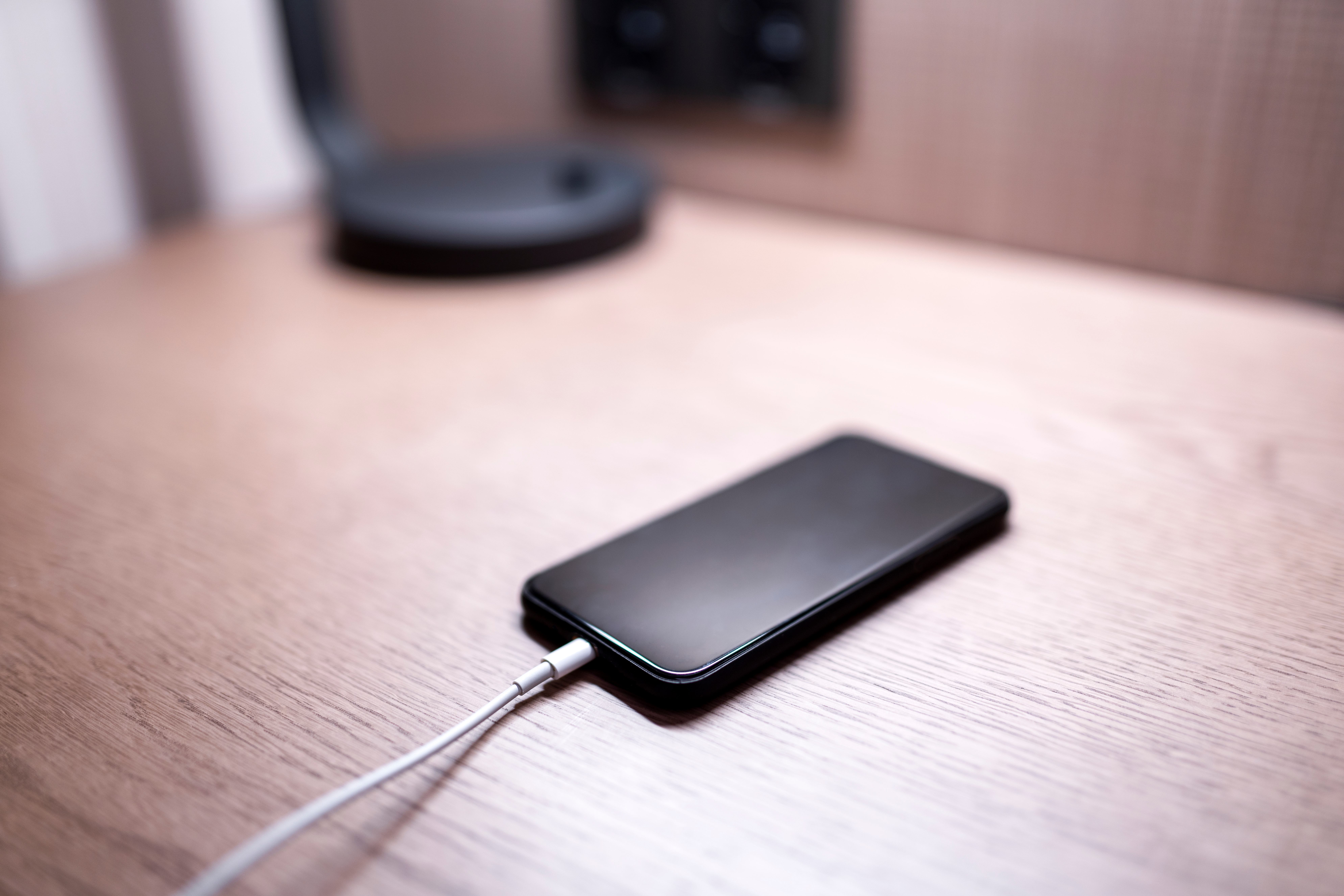 Smarttelefonlading på et trebord, med en uskarp lampe i bakgrunnen