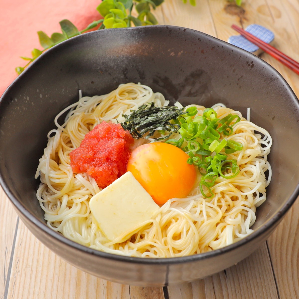 黒い器に盛られた冷麺。トッピングは玉子、明太子、海苔、刻みネギ、バター。