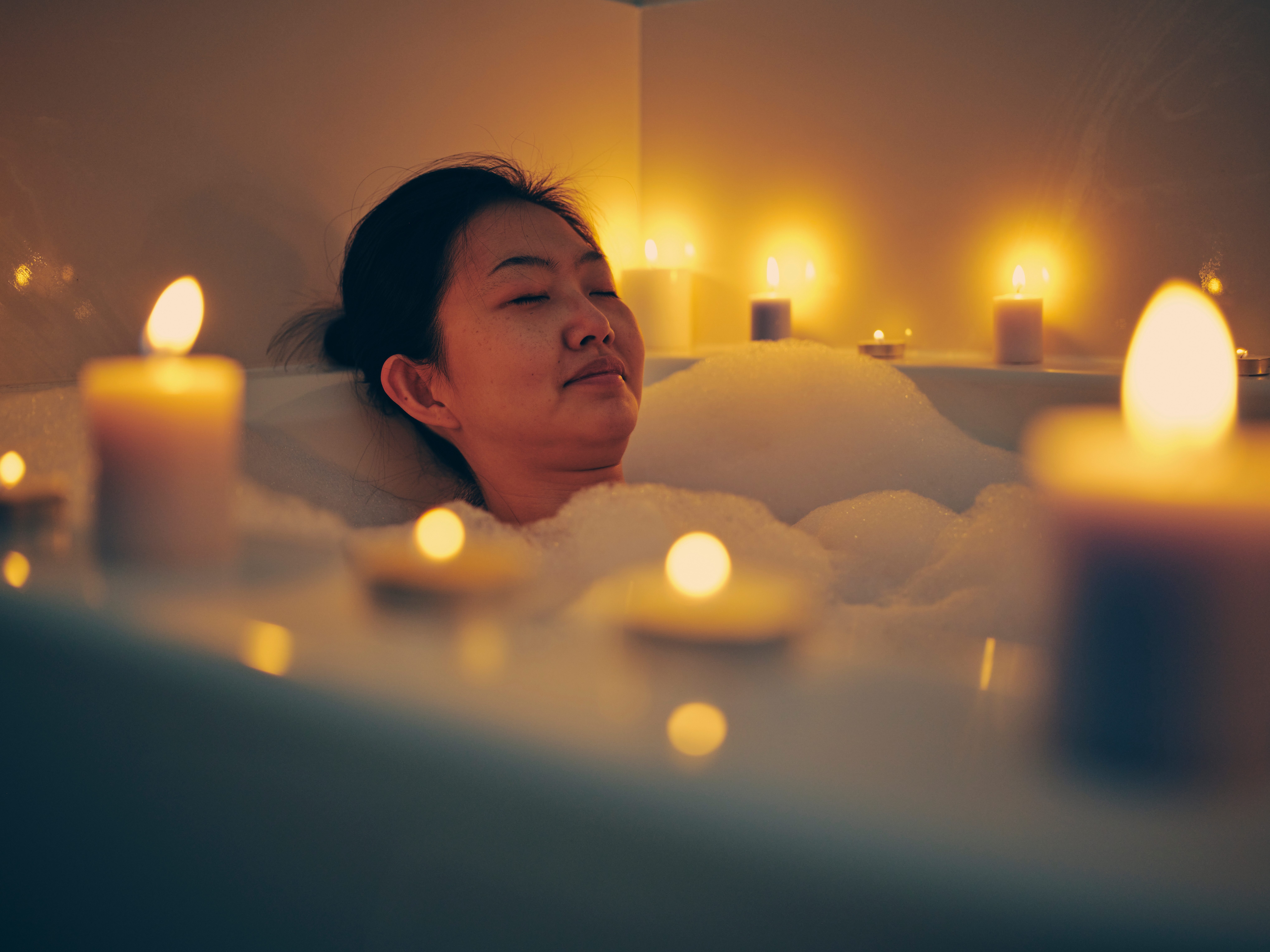 Person slapper av i et boblebad omgitt av tente lys, lukkede øyne, formidler en følelse av fred og ro