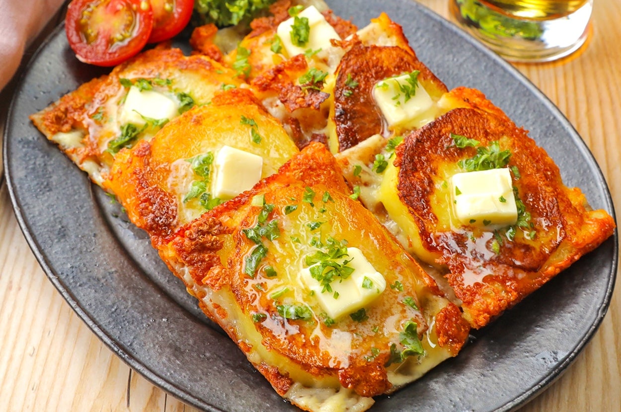 クリスピーに焼かれたチーズトーストが黒い皿に乗っている。バターが溶け、パセリとトマトが添えられている。