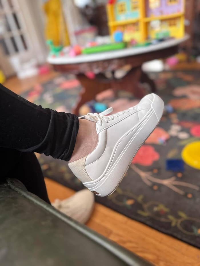 Person wearing achromatic sneakers with achromatic leggings, sitting indoors. Background shows children's toys and colorful play area