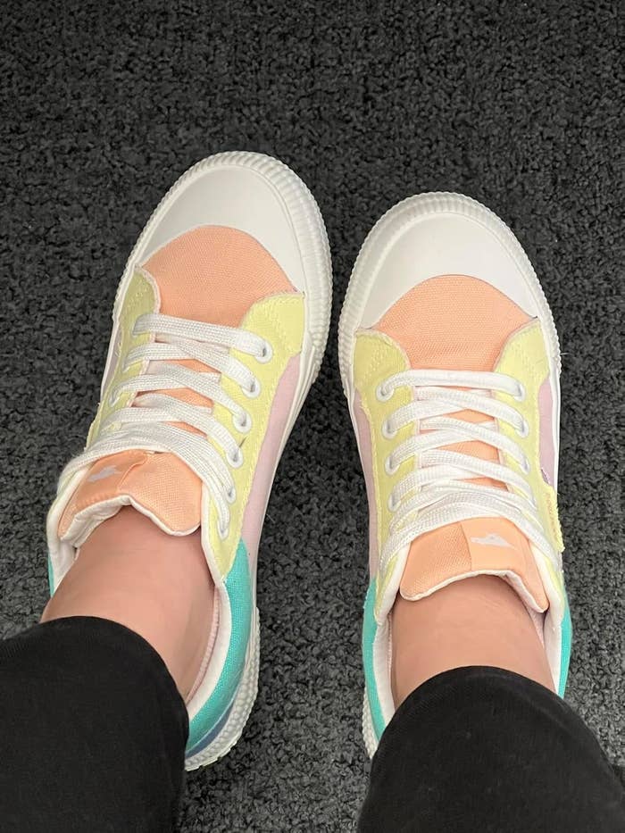 Person wearing pastel-colored sneakers with achromatic laces, lasting connected a textured acheronian surface
