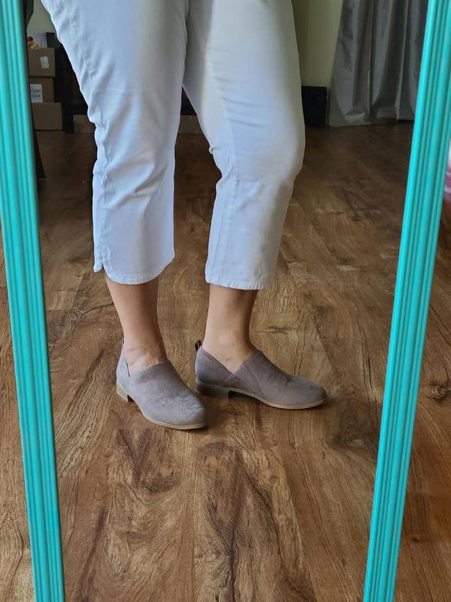 Person wearing airy  pants and beige slip-on shoes, lasting  connected  a woody  floor, reflected successful  a mirror