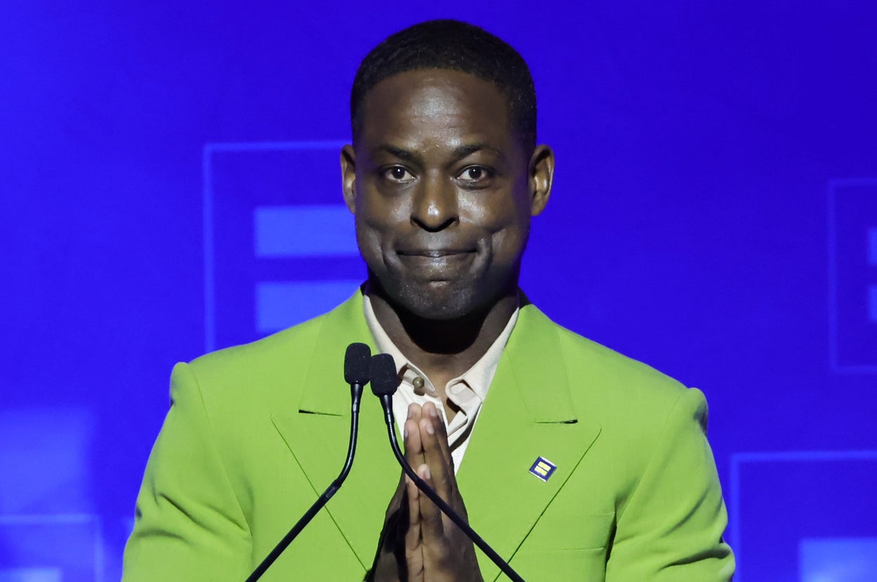 Sterling K Brown in a suit speaks at a podium during a Human Rights Campaign event, with hands clasped in front of them