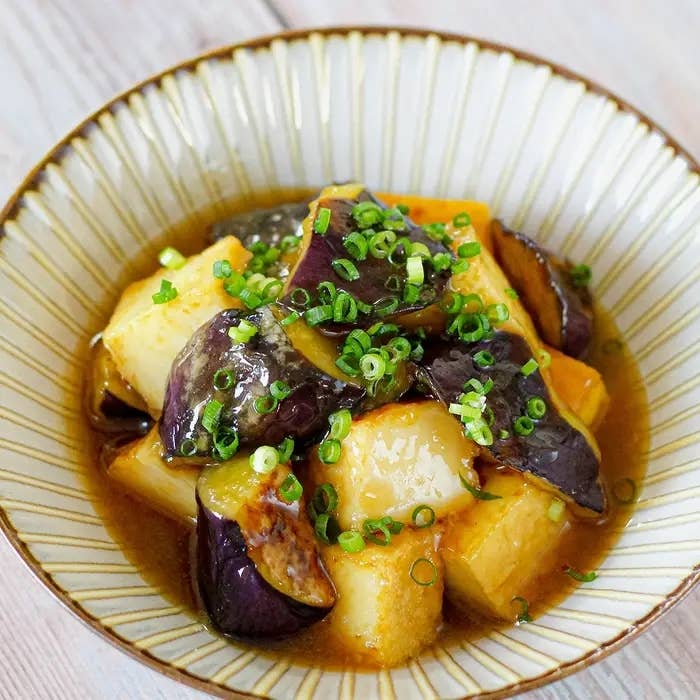 茄子と豆腐の煮物が皿に盛られている。青ネギがトッピングされている。