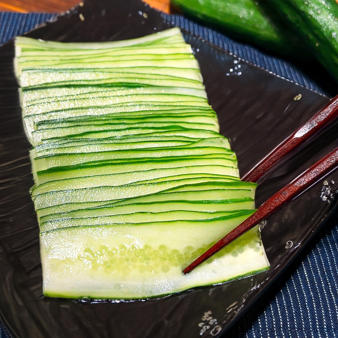 薄くスライスされたキュウリ数枚が、箸と共に皿に整然と並べられた料理。
