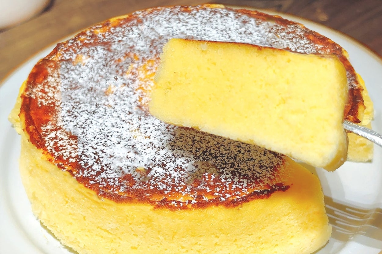 ふわふわのチーズケーキが皿にのっており、上に軽く粉砂糖が振りかけられています。一切れがカットされています。