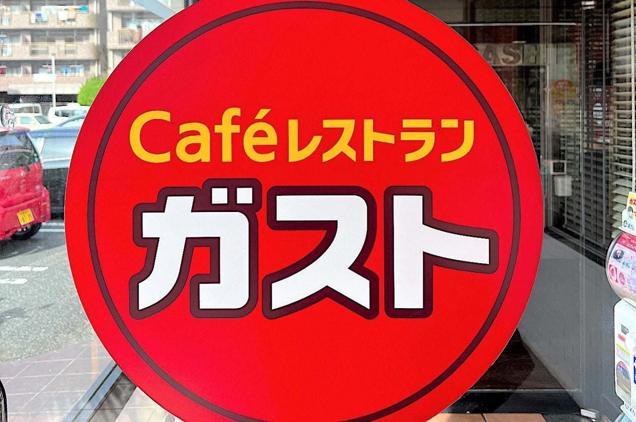 Sign with "Café Restaurant Gasto" in Japanese, displayed on a glass door of a café, with street background visible