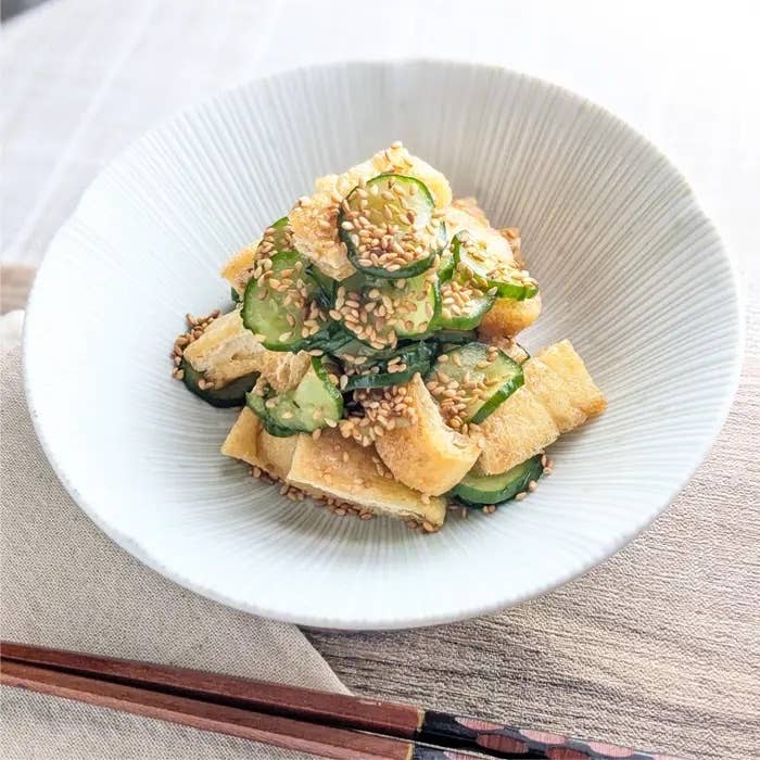 白い皿に盛られたキュウリと揚げの和え物。ゴマが振りかけられている。箸が添えられている。