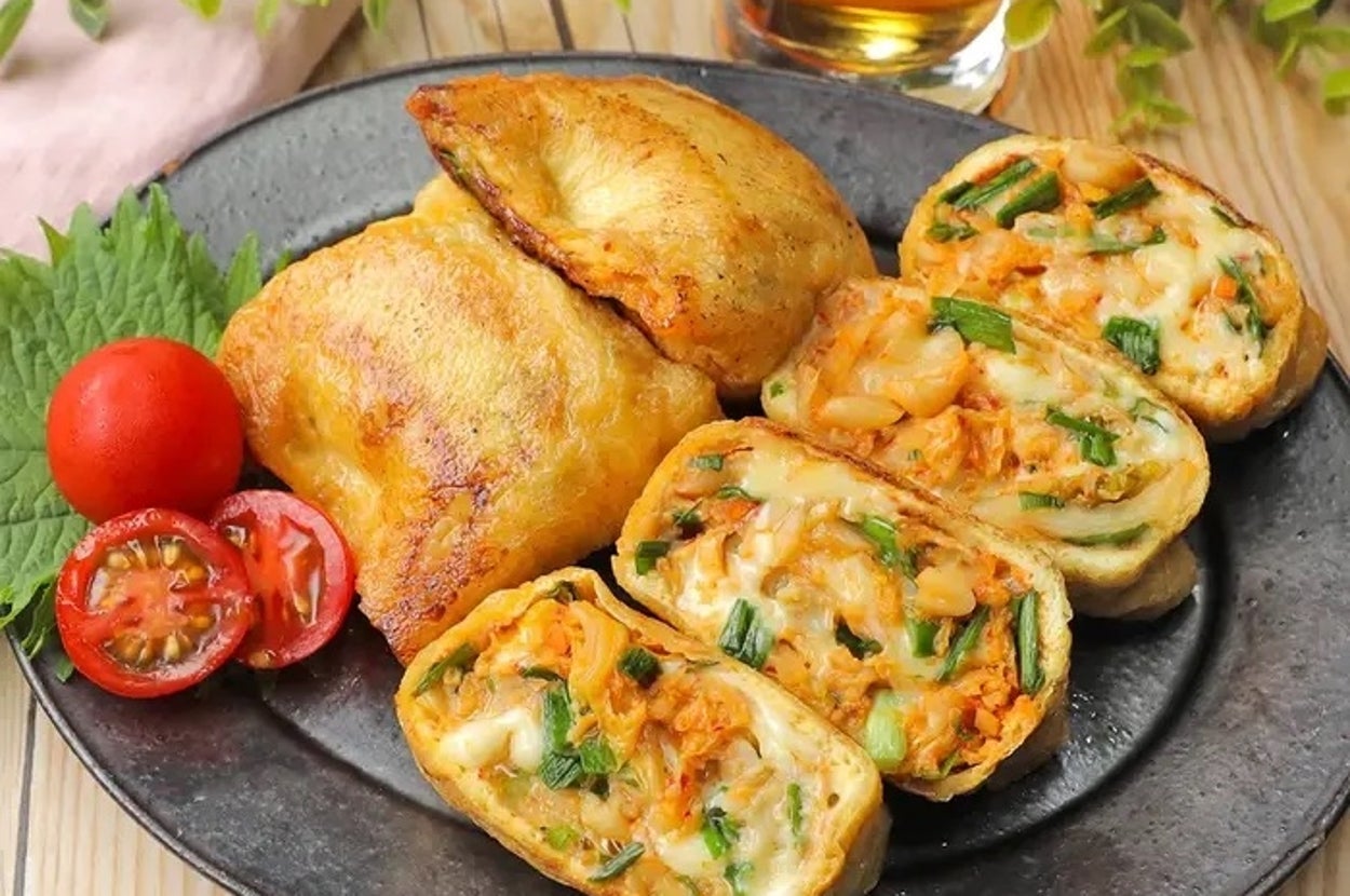 皿に盛られたおいなりさんのアレンジ料理。野菜やチーズが詰まっており、トマトと飲み物が添えられている。