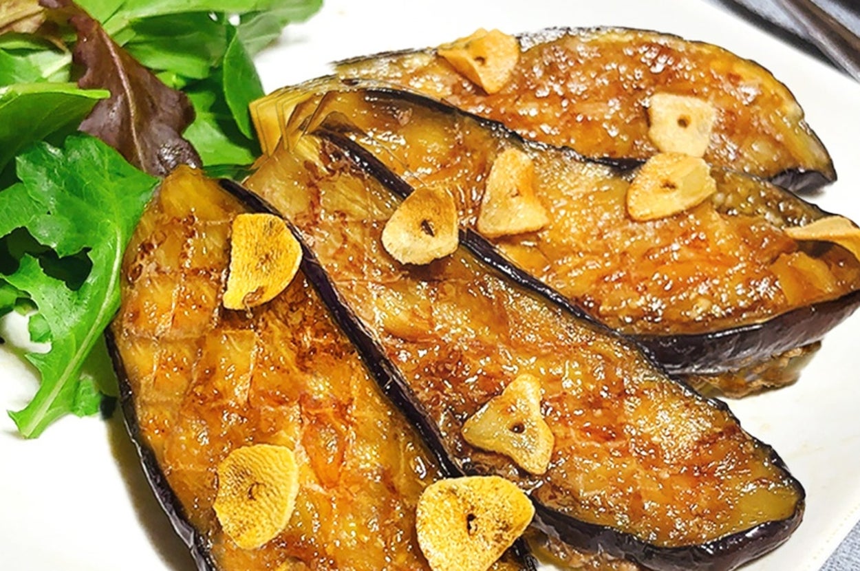 皿に盛られた焼きナスとスライスされたにんにく、付け合わせに葉物野菜。