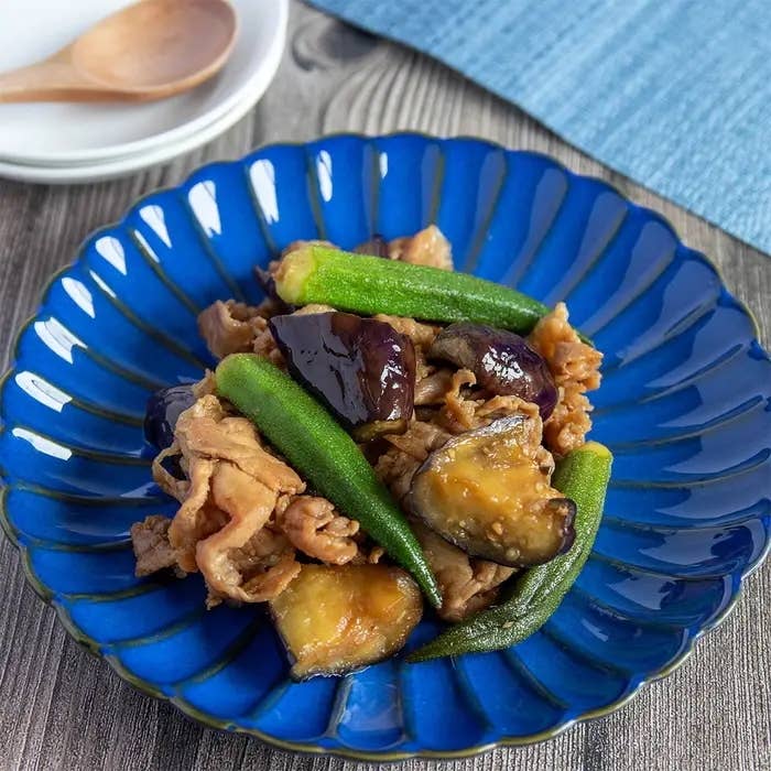 青い皿に盛られた野菜と肉の料理。オクラとナス、薄切りの肉が目立つ。